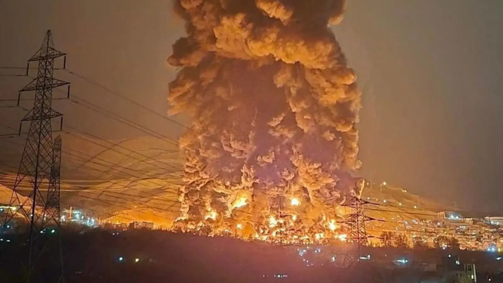 一根巨大的火焰和烟柱在夜晚的城市爆炸后升起，附近还能看到电线